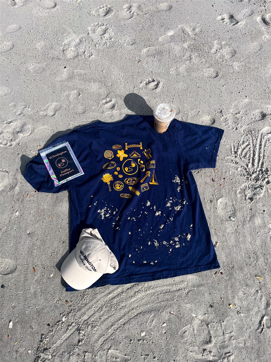 Wilmington Coffee Passport T-Shirt, navy, with passport and hat on sand